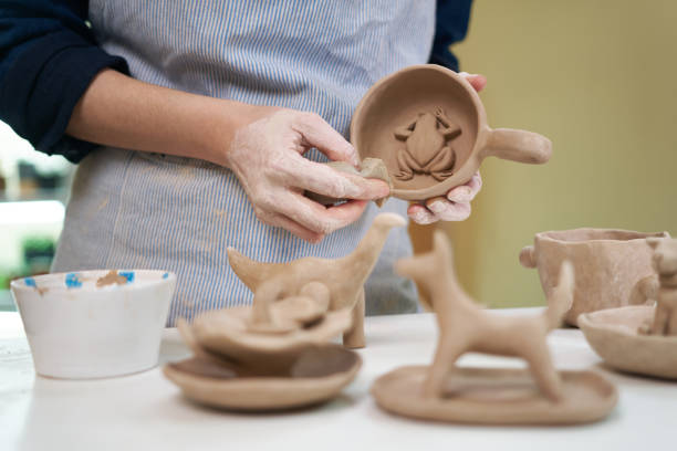 woman forming clay cup shape by hands, closeup in artistic studio.