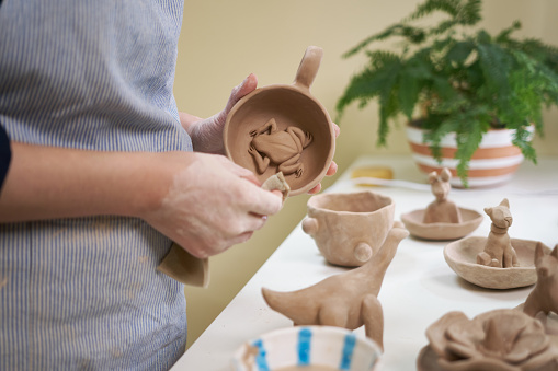 woman forming clay cup shape by hands, closeup in artistic studio.