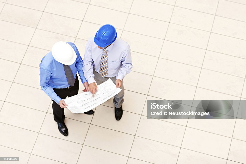 Professionals Looking Over Blueprints "Overhead view of two professionals in hardhats, looking over a set of blueprints. Horizontal shot." Directly Above Stock Photo