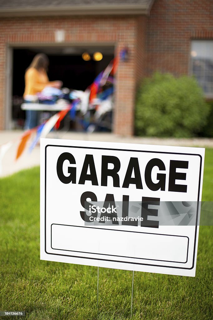Garage Sale Sign with Girl Shopping Garage sale sign on the front yard of a suburban house with a woman looking at items on a table. Garage Sale Stock Photo