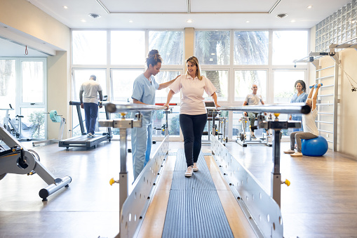 Woman in physical therapy walking on the bars at a rehabilitation center - orthopedic medicine concepts