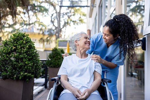 Happy home caregiver helping a senior woman in a wheelchair and smiling at her - assisted living concepts