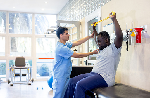 African American man doing physical therapy using a resistance band with the assistance of his therapist - orthopedic medicine concepts