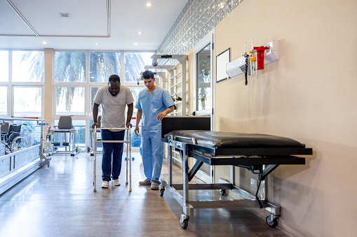 Mature man in physical therapy trying to walk using a walker with the help of his therapist - orthopedic medicine concepts