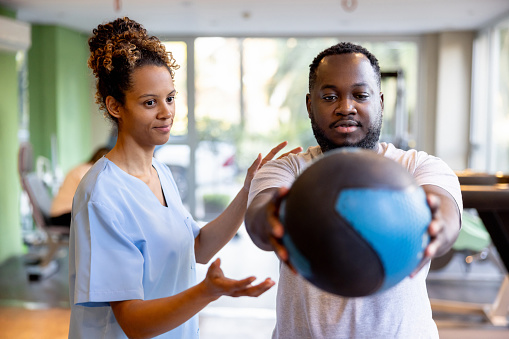 African American man doing physical therapy using a fitness ball with the assistance of his therapist - orthopedic medicine concepts