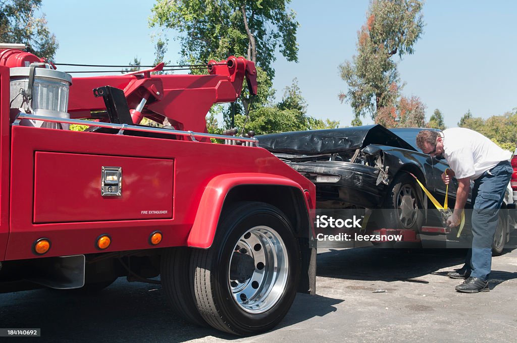 Tow Truck Driver Hauling a Wrecked Car Tow truck driver securely strapping a wrecked car in preparation for towing it. Tow Truck Stock Photo