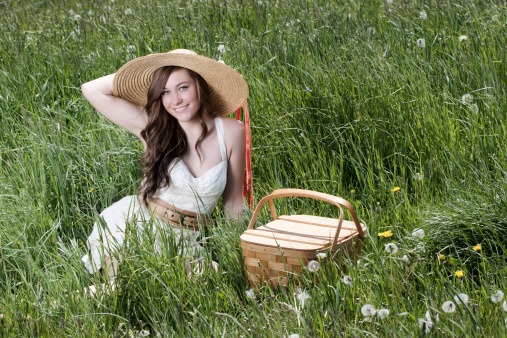 Beautiful young woman with picnic basket. Wearing a straw summer hat outdoors.