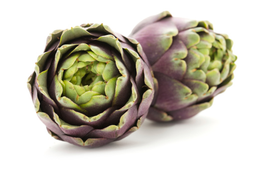 A purple flower of a globe artichoke is in full bloom, beside it are other artichoke heads that have not yet flowered.