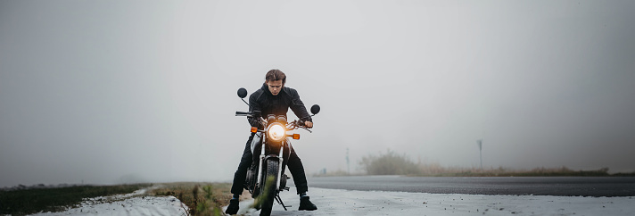 male motorcyclist with a motorcycle on a foggy asphalt road.