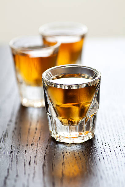 Whiskey shots Three shot glasses full of dark colored alcohol on top of a bar table. The shot could be whiskey, dark rum, tequila, cognac, or bourbon. SHOT OF RUM stock pictures, royalty-free photos & images