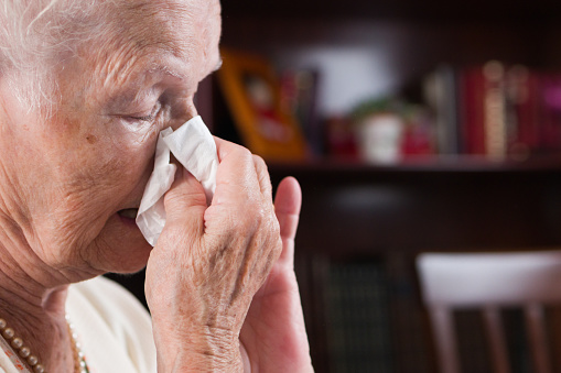 close up of old woman blowing snot from her nose with a tissue.fever and illness due to respiratory disease caused by the influenza virus at home.image with copy space