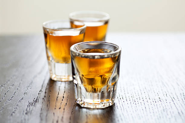 Whiskey shots Three shot glasses full of dark colored alcohol on top of a bar table. The shot could be whiskey, dark rum, tequila, cognac, or bourbon. SHOT OF RUM stock pictures, royalty-free photos & images