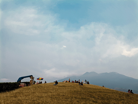 Karanganyar, Indonesia - October 21, 2023: People sat enjoying the beauty of nature on a green grassy hilltop. Relaxing and spending time in nature.