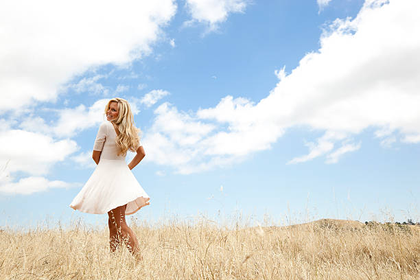 smiling young woman twirling her skirt in field of dried grass
