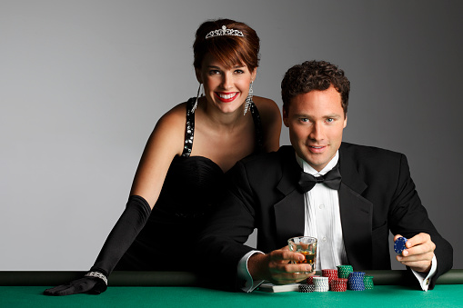 A man and a woman in formal attire at a roulette table with their gambling chips while smiling and looking at the camera.