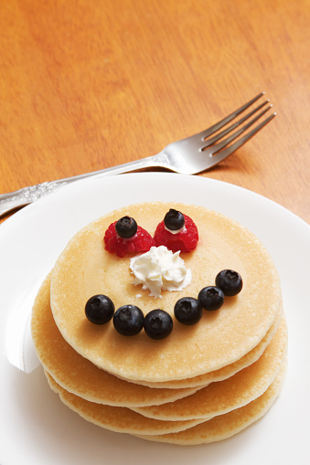 a plate of pancakes with a funny face made of fruit and cream. 
