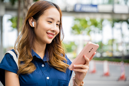 Young woman talking on her smartphone and wearing earbuds while walking outside. This portrait shows a person's modern lifestyle.