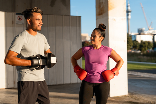 Pacific Islander couple in casual clothing wearing boxing gloves taking a break from training.