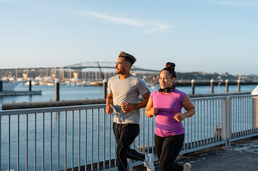 Happy Pacific Islander couple together jogging outdoors in casual clothing.