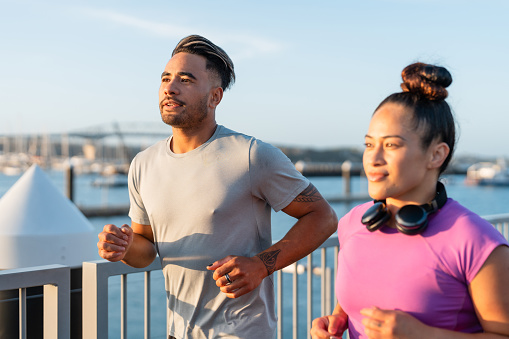 Happy Pacific Islander couple together jogging outdoors in Auckland City with Harbor bridge in background.