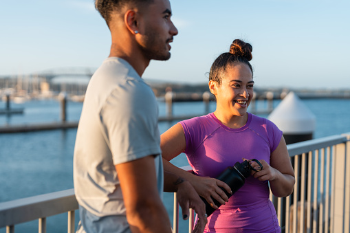 Happy Pacific Islander couple outdoors gossiping and taking rest after workout.