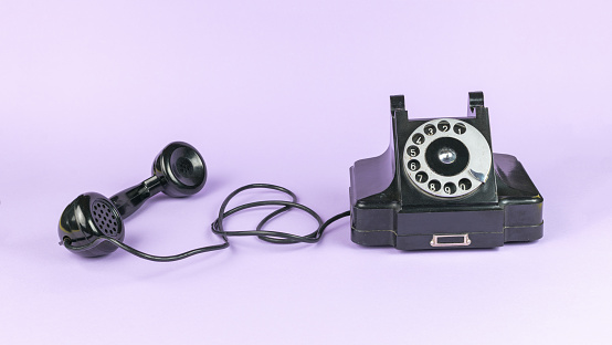 Black vintage handset with the handset off on a purple background. The old technique.