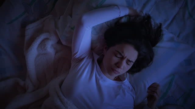 Low key top down turning view of Hispanic woman suffering from insomnia lying down on the bed.