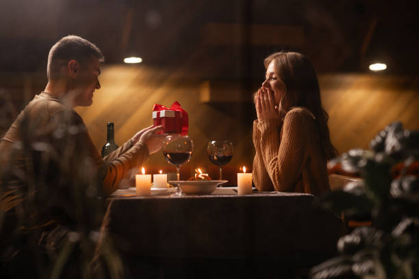 istock Romantic date concept. Handsome boyfriend giving gift for girlfriend while celebrating Valentine's Day in restaurant or home. 1841754087