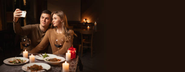 istock Happy couple in love having dinner, celebrating Valentines Day and taking selfie using smartphone in the night at home. Banner. 1841754598