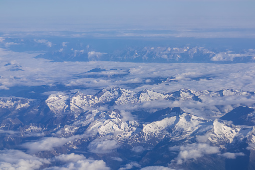 Window view from an airplane on the snow capped mountain ranges of the Alps at the border Austria Italy, Europe, EU. High peak are shrouded in clouds. Flying high above the ground. Freedom