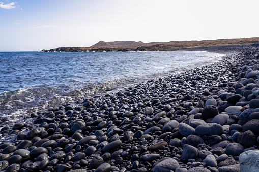 Panoramic view on black stone pebble beach Playa Colmenares near Amarilla, Golf del Sur, Tenerife, Canary Islands, Spain, Europe. Montana Amarilla in the back. Tranquil waves from the Atlantic Ocean