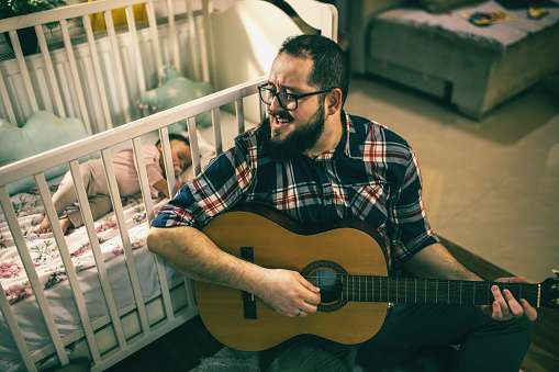 a young father lulls his baby to sleep while playing the guitar and singing