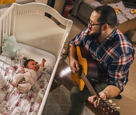 a young father lulls his baby to sleep while playing the guitar and singing