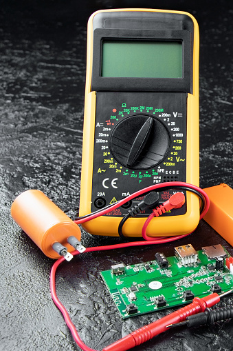 Digital multi-meter with probes on a black stone background. Multitester and microcircuit. Voltage Tester. Copy space. Voltmeter. Measuring tool. DMM