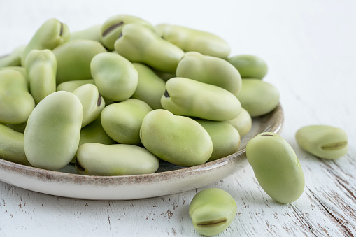 broad beans, closeup side view delicious fresh raw organic green broad beans on plate on wooden table or background. fresh superfood. raw vegetarian ingredients. healthy food concept on white surface