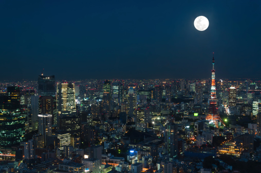 The cityscape of Tokyo at night, beneath a full moon.