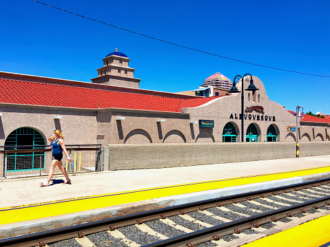 Albuquerque, New Mexico, USA - July 31, 2020: A woman carrying a young child walks past the Alvarado Transportation Center (ATC), a transportation hub for bus, passenger rail, and commuter trains.