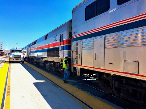 Albuquerque, New Mexico, USA - July 31, 2020: An Amtrak employee checks connections as a fuel truck driver completes refueling Amtrak’s Southwest Chief passenger train during a scheduled stop at the Alvarado Transportation Center (ATC) that serves as the city’s Amtrak station.