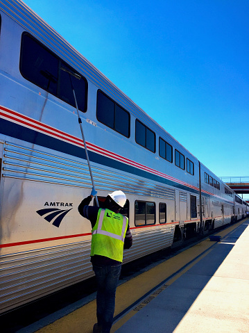 Albuquerque, New Mexico, USA - July 31, 2020: An Amtrak employee washes the windows of Amtrak’s Southwest Chief passenger train during a scheduled stop at the Alvarado Transportation Center (ATC) that serves as the city’s Amtrak station.