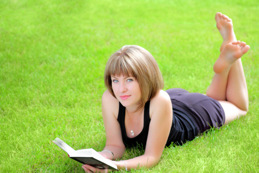 outdoor picture of lovely student girl with book on the fresh grass