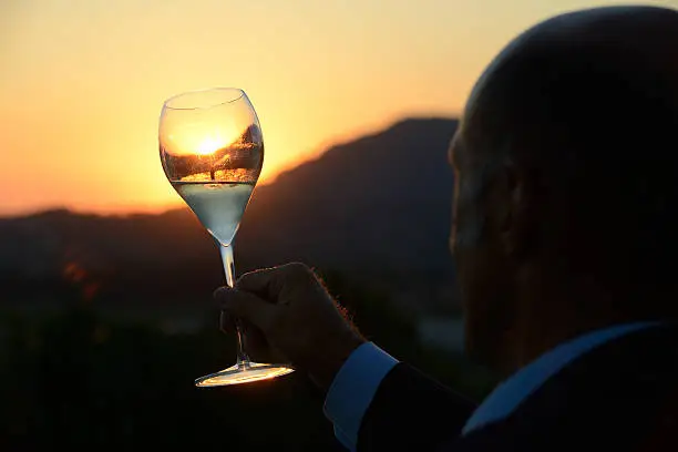 Man is looking at a glass of sparkling wine at sunset