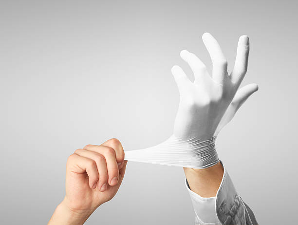 Stretching a white rubber glove over the left hand Doctor dress gloves on hands on gray background formal glove stock pictures, royalty-free photos & images