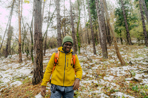 Photo of a young man having a walk with a backpack through beautiful nature on a cold and snowy winter day.