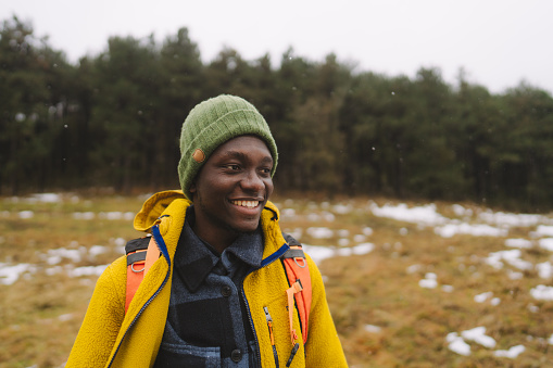 Photo of a young man having a walk with a backpack through beautiful nature on a cold and snowy winter day.