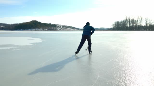 Senior man with hockey stick skating on ice in winter.