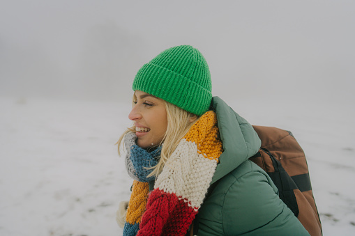 Photo of a young woman having a walk with a backpack through beautiful nature on a cold and snowy winter day.