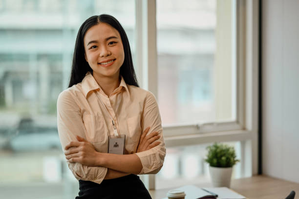 Portrait of a young Asian female employee standing with arms crossed and looks at the camera with a smile stock photo