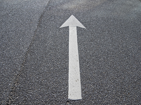 A white arrow on black asphalt pointing straight ahead.