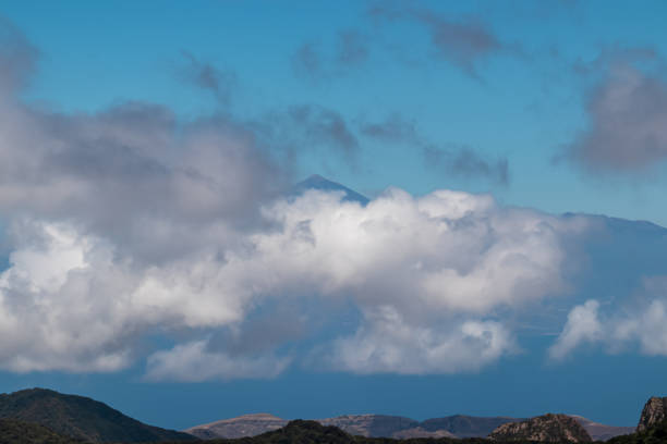 Scenic view on the cloud covered volcano mountain peak Pico del Teide on Tenerife seen from La Gomera, Canary Islands, Spain, Europe. Mystical magical atmosphere on hiking trail to Roque de Agando