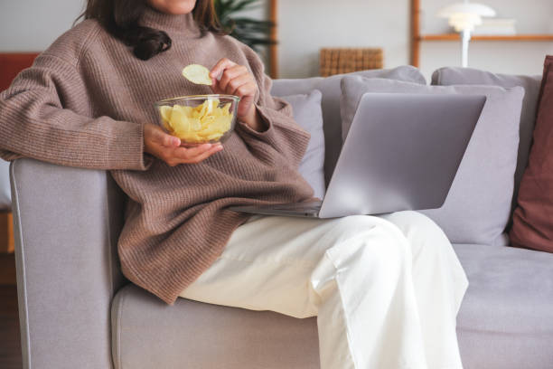 istock Closeup image of a young woman eating potato chips while watching on laptop computer at home 1842096019